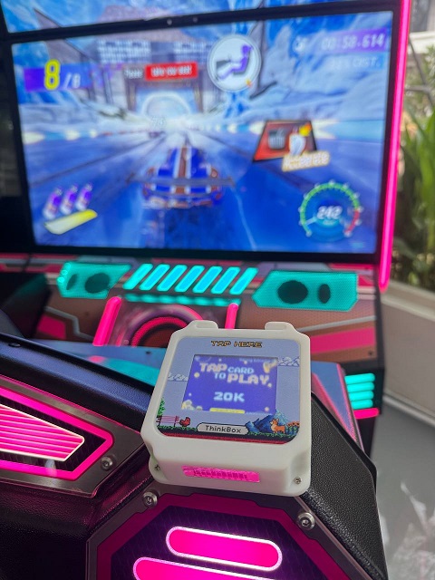 Thiết bị ThinkBox Arcade Cashless gắn trên máy arcade — chạm thẻ để chơi